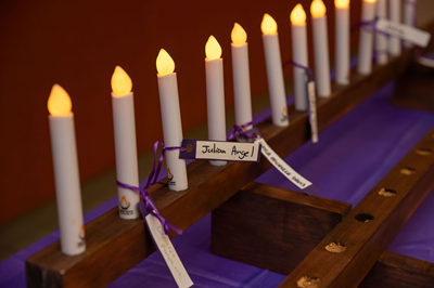 A row of candles with nametags tied to them in purple ribbons.